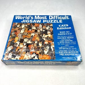 May include: A sealed jigsaw puzzle box titled "World's Most Difficult Jigsaw Puzzle: Cats Edition." The puzzle features a collage of numerous cats in various colors and patterns. The box text explains the puzzle is double-sided.