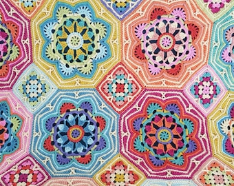 May include: A multicolored crochet blanket featuring a repeating pattern of large, intricate floral-shaped motifs in shades of pink, yellow, blue, orange, and purple, connected by smaller square-shaped crochet segments in a dense, textured yarn.