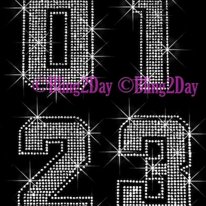 May include: A set of three rhinestone numbers, 0, 1, and 2, in a silver color. The numbers are made of small, round rhinestones that are arranged in a geometric pattern. The numbers are set against a black background.