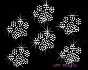 May include: Five silver glitter paw prints on a black background.  The paw prints are made of small, round rhinestones.