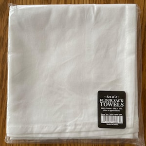 May include: A package containing two white flour sack towels. The towels are made of 100% cotton and measure approximately 28 inches by 29 inches. The package includes a label that reads "Flour Sack Towels."
