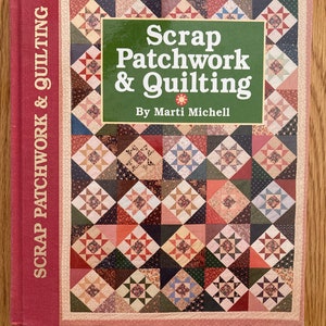 May include: A hardcover book titled "Scrap Patchwork & Quilting" by Marti Michell. The book cover features a patchwork design with various fabric patterns in shades of red, pink, blue, and green. The spine of the book is a solid red color.