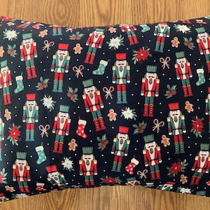 May include: Rectangular pillow with a dark blue background covered in a repeating pattern of nutcrackers, gingerbread men, candy canes, stockings, and poinsettias. The nutcrackers are in red, green, and white.