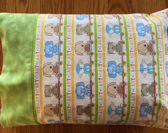 May include: A rectangular baby pillowcase with a green border and a pattern of cartoon animals on skateboards. The pattern includes bears, dogs, and elephants in blue, brown, and tan colors. The word "BABY" is printed repeatedly.
