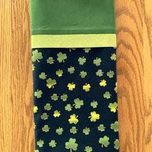 May include: A green and navy blue pillowcase with a shamrock pattern. The top of the pillowcase is solid green, with a lighter green band separating it from the navy blue shamrock print. The shamrocks are in shades of green and yellow.