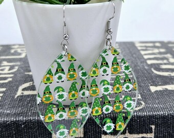 May include: A pair of dangle earrings with a clear, teardrop-shaped design. The earrings feature a pattern of green gnomes with white beards and green hats, wearing shamrocks. The earrings have silver hooks.