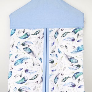 May include: A light blue diaper caddy with a white background and a watercolor feather pattern. The caddy has a blue ribbon down the center and a blue top with a hanger.