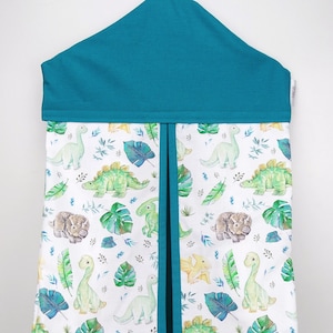 May include: A turquoise diaper caddy with a white background featuring a pattern of green dinosaurs and tropical leaves. The caddy has a pocket on the front and a hanging loop on the top.