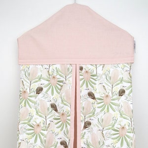 May include: A pink and white diaper caddy with a floral print featuring birds and flowers. The caddy has a pink flap on top and a hanging loop.