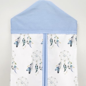 May include: A white diaper caddy with a blue top and a dreamcatcher and feather pattern. The caddy has a blue trim and a hanger.