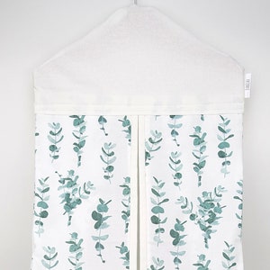 May include: White hanging diaper caddy with a eucalyptus leaf pattern. The caddy has a flap that opens and closes.