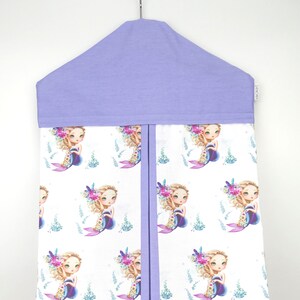 May include: A lavender diaper caddy with a white background featuring a repeating pattern of mermaids with floral crowns. The caddy has a hanging loop and a zipper closure.