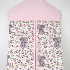 May include: Pink diaper caddy with a floral print featuring grey elephants wearing crowns. The caddy has two compartments and a pink hanger.