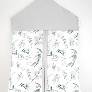 Puede incluir: Un organizador de pañales gris y blanco con un patrón floral que presenta hojas verdes y bayas marrones. El organizador tiene una parte superior gris con un colgador y una etiqueta que dice "ORGANIZE".