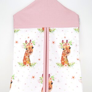 May include: Pink diaper caddy with a white floral print featuring giraffes wearing flower crowns. The caddy has a pink top and a hanging loop.