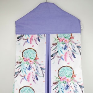 May include: A purple fabric diaper caddy with a white background featuring a repeating pattern of dreamcatchers, feathers, and flowers. The caddy has a flap at the top that can be folded down.