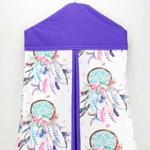 May include: Purple diaper caddy with a white background featuring a repeating pattern of dreamcatchers with feathers and flowers. The caddy has a pocket on the front and a hanging loop.