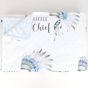 Puede incluir: Una manta de beb&eacute; blanca con un patr&oacute;n de tocado azul y blanco. La manta tiene las palabras "Little Chief" impresas.