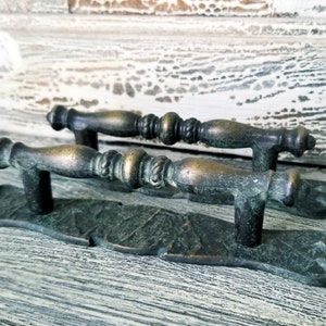 May include: Two antique bronze cabinet door pulls with ornate detailing. The pulls are attached to a decorative metal plate.
