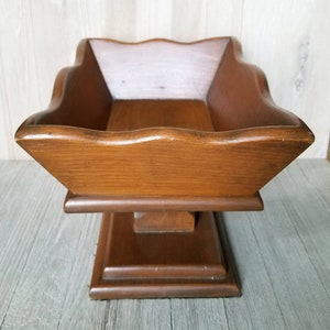 May include: A wooden serving tray with a scalloped edge and a pedestal base. The tray is made of dark brown wood and has a natural finish.