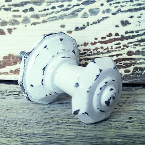 May include: White metal cabinet knob with a distressed finish. The knob has a hexagonal shape and a raised center.
