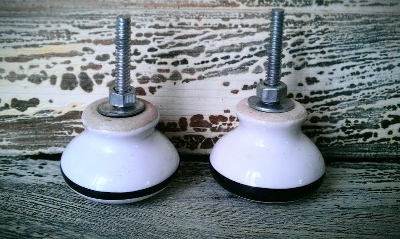 May include: Two white ceramic cabinet knobs with black trim and silver metal accents. The knobs have a screw-on design.