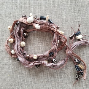 May include: A brown silk cord bracelet with white and black beads. The cord is tied in a knot at the end.