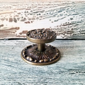 May include: Antique brass cabinet knob with a floral design. The knob has a round top and base with intricate detailing. The hardware is likely made of metal and is suitable for furniture restoration or decorative projects.