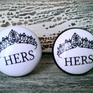 May include: Two white oval ceramic knobs with black crown and the word "HERS" printed on them.