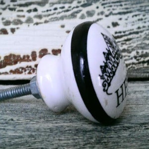 May include: White ceramic knob with a black stripe and a black and white design of a city skyline. The knob has a silver screw.