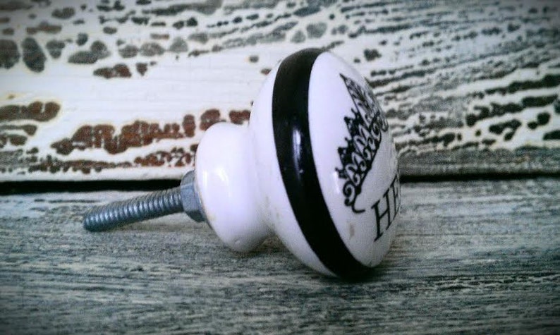 May include: White ceramic knob with a black stripe and a black and white design of a city skyline. The knob has a silver screw.