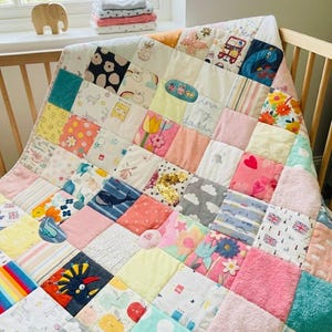 May include: A patchwork baby quilt featuring a variety of colorful fabric squares with diverse patterns including flowers, whales, clouds, rainbows, and hearts. The quilt includes embroidered details, sequins, and text reading love my daddy.