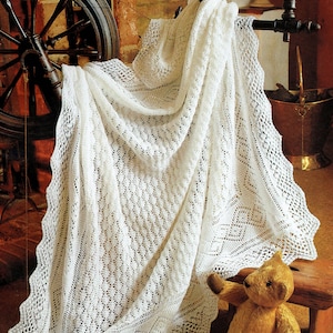 May include: A white crocheted baby shawl with a delicate lace pattern, draped over a spinning wheel and a teddy bear. The shawl is 127 cm square and is made with 3 ply yarn.
