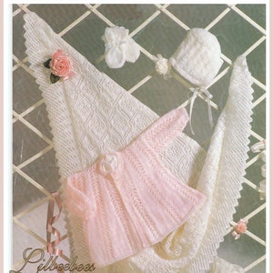 May include: A knitted baby set including a shawl, matinee jacket, bonnet, mittens, and booties. The set is primarily white with a pink jacket. The shawl measures 107 cm. The text on the image reads "Shawl, Matinee Jacket, Bonnet, Mittens & Bootees."