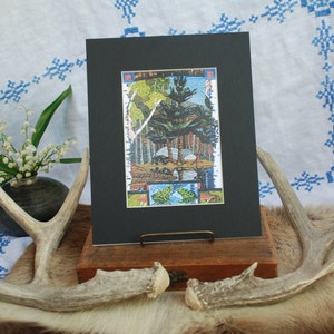 May include: A framed print of a colourful, abstract landscape with trees and geometric shapes. The print is matted in black and has a wooden frame.