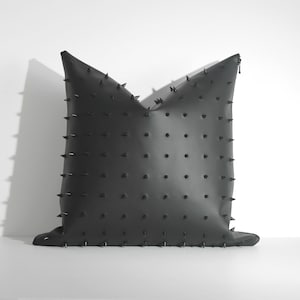 May include: A black pillow with a zip closure and a pattern of small, black spikes.
