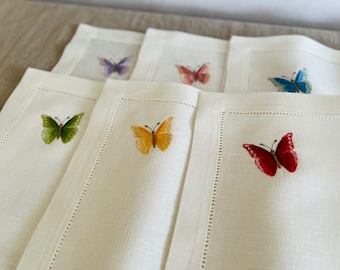 May include: Set of six white linen placemats with embroidered butterflies in various colors, including green, yellow, pink, purple, blue, and red.