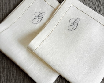 May include: Two white linen napkins with a single embroidered letter "G" in a script font on each.