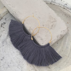 May include: A pair of hoop earrings with gray tassel fringe. The hoops are gold-toned metal.