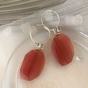 May include: A pair of gold hoop earrings with a red, faceted gemstone pendant and a white ceramic bead with black markings.