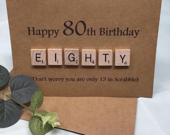 May include: A brown card with the text "Happy 80th Birthday" and the word "EIGHTY" spelled out with Scrabble tiles. The card also includes the text "Don't worry you are only 13 in Scrabble".