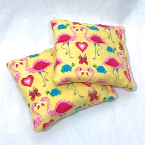 May include: Two yellow fabric squares with pink flamingos, butterflies, and turtles. The fabric is soft and has a subtle texture.