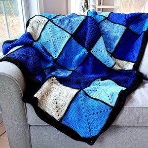 Puede incluir: Una manta de crochet azul y blanca con un patrón de diamantes. La manta está colocada sobre un sofá gris.