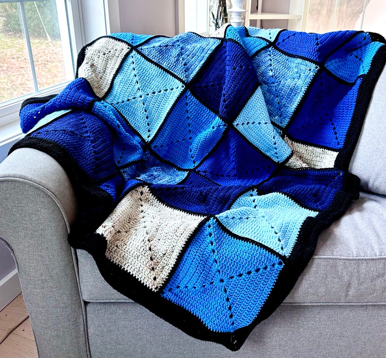 以下が含まれることがあります： ダイヤモンド柄の青と白の編み物毛布。毛布は灰色のソファにかけられています。