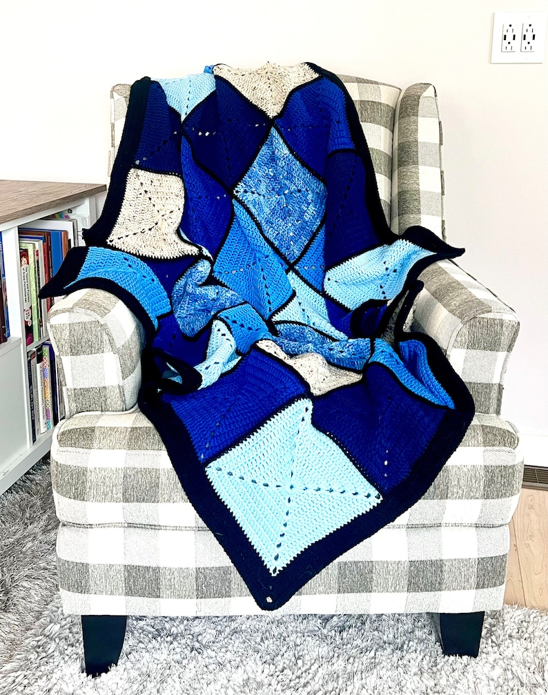 以下が含まれることがあります： グレーと白のチェック柄の肘掛け椅子に、青、白、グレーのダイヤモンド柄のクロシェ編み毛布がかけられています。