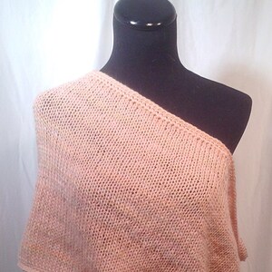 May include: A peach-colored knitted shawl with a one-shoulder design. The shawl is draped over a black mannequin.