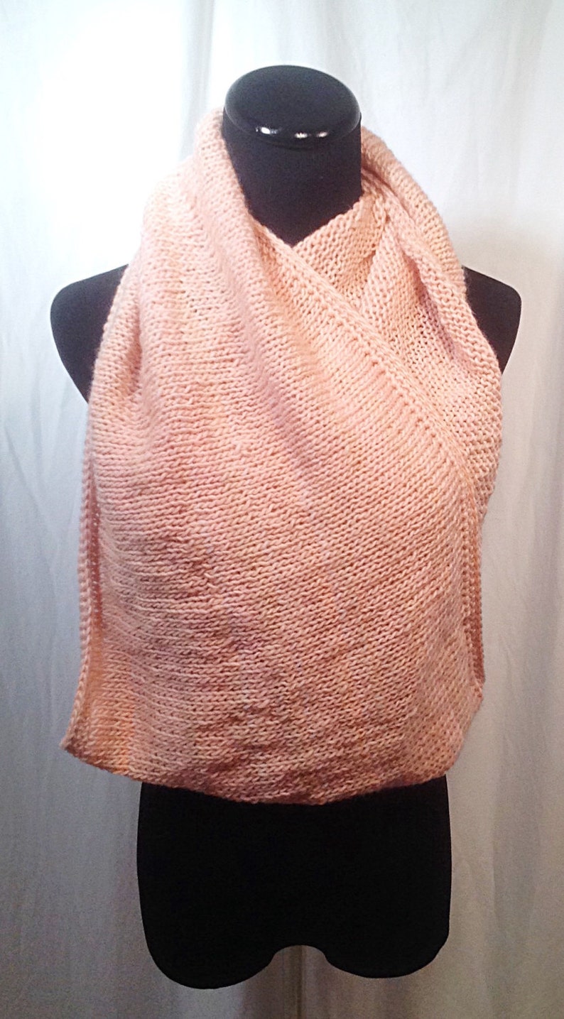May include: A soft, peach-colored knitted scarf. The scarf is draped over a black mannequin.