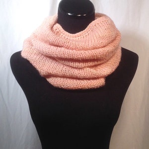May include: A soft, peach-colored knitted infinity scarf. The scarf is folded and displayed on a black mannequin.