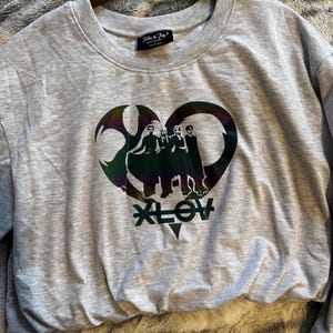 May include: A light gray sweatshirt with a crew neck and long sleeves. The front features a heart-shaped graphic with a band silhouette and the word "XLOV" below. The brand tag "Jolie & Joy" is visible at the neckline.
