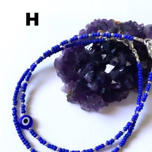 May include: A blue and silver beaded bracelet with a blue evil eye charm. The bracelet is on a purple amethyst crystal.